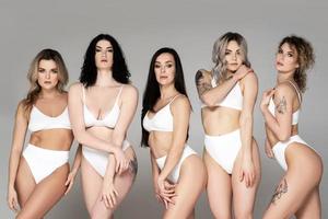 Group of different women wearing  white lingerie on gray background. photo