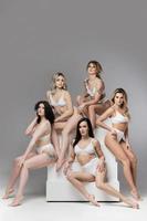 Group of different women wearing  white lingerie on gray background. photo