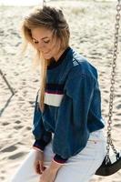 Young smiling woman sitting on the swing at the sandy beach. photo