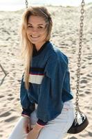 Young smiling woman sitting on the swing at the sandy beach. photo