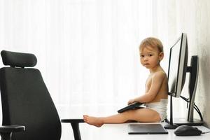 Little boy sitting on a desk and playing with a keyboard. photo