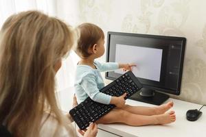 Little boy sitting on a desk and distracting mother from work on computer. photo