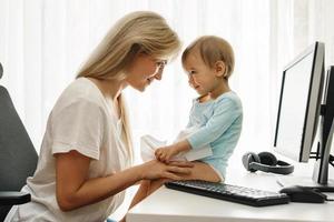 Little boy sitting on a desk distracting freelancer mother from paperwork. photo