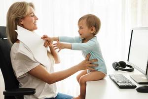 Little boy sitting on a desk distracting freelancer mother from paperwork. photo