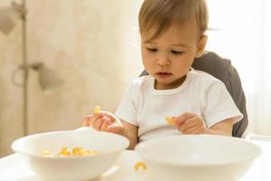 Cute little boy on a high chair playing with pasta. photo