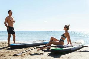 Male and female standup paddleboard surfers relaxing on a beach. photo