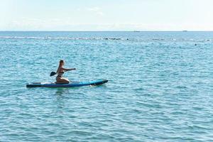 joven surfista en bikini montando paddleboard de pie en el océano. foto