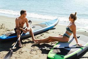 Male and female standup paddleboard surfers relaxing on a beach. photo