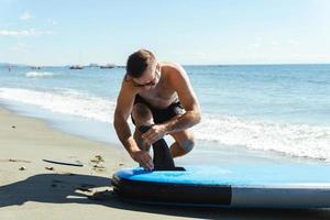 Young male surfer setting up standup paddleboard on a beach. photo