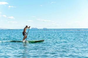 Young male surfer riding standup paddleboard in ocean. photo