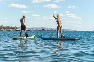 surfistas masculinos y femeninos montando paddleboards de pie en el océano. foto