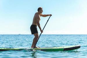 Young male surfer riding standup paddleboard in ocean. photo