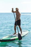 Young male surfer riding standup paddleboard in ocean. photo