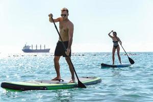 surfistas masculinos y femeninos montando paddleboards de pie en el océano. foto