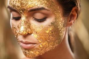 hermosa mujer con máscara dorada brillante en la cara para el tratamiento de la piel