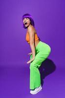 Carefree woman wearing colorful sportswear twerking against purple background photo