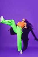 Active woman dancer wearing colorful sportswear performing against purple background photo