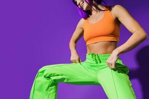 Carefree woman dancer wearing colorful sportswear having fun against purple background photo