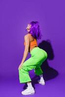 Carefree woman wearing colorful sportswear twerking against purple background photo