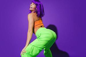 Carefree woman wearing colorful sportswear twerking against purple background photo