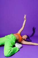 Carefree woman dancer wearing colorful sportswear performing against purple background photo