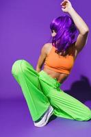 Carefree woman dancer wearing colorful sportswear performing against purple background photo