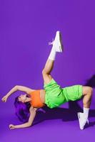 Carefree woman dancer wearing colorful sportswear performing against purple background photo