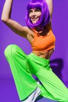 Carefree woman dancer wearing colorful sportswear performing against purple background photo