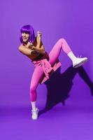 Carefree woman dancer wearing colorful sportswear performing against purple background photo