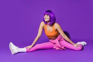 Cheerful woman wearing colorful sportswear sitting against purple background photo