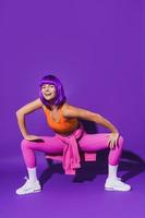 Carefree woman dancer wearing colorful sportswear performing against purple background photo