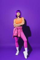 Cheerful woman wearing colorful sportswear sitting against purple background photo