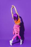 Carefree woman dancer wearing colorful sportswear performing against purple background photo