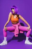 Carefree woman dancer wearing colorful sportswear performing against purple background photo