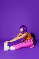 mujer alegre que usa ropa deportiva colorida durante el entrenamiento de estiramiento contra el fondo púrpura foto