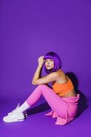 Young woman wearing colorful sportswear sitting against purple background photo