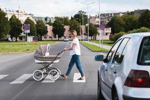 Young mother with the baby pram is walking by the crosswalk photo