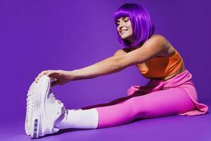 cheerful woman wearing colorful sportswear during stretching workout against purple background photo