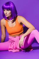 Young woman wearing colorful sportswear sitting against purple background photo