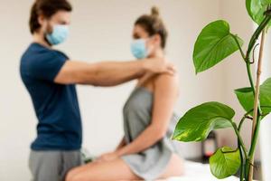 Man manual therapist wearing prevention mask is working with a woman client photo