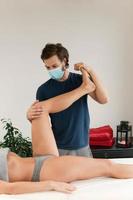 Manual therapist wearing prevention mask is working with a client in the massage clinic photo