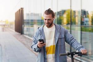 Man with e-scooter using  scooter-sharing system application on his smartphone photo