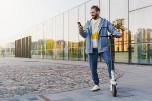 hombre alegre con e-scooter usando la aplicación del sistema de uso compartido de scooters en su teléfono inteligente foto