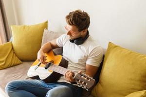 Young man on sofa is playing acoustic guitar photo