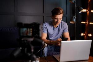 Young blogger is using his phone in front of a laptop photo