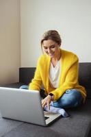 mujer con cárdigan amarillo sentada en el sofá y usando una computadora portátil foto