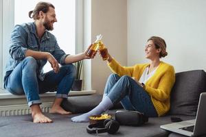 Young cheerful couple sitting on the sofa drinking beer and eating nachos photo