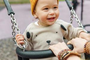 Cute baby boy sitting on a swing in public park photo