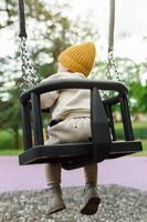 Cute baby boy sitting on a swing in public park photo