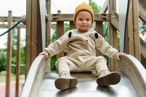 Cute baby boy sitting on playground slide in public park photo